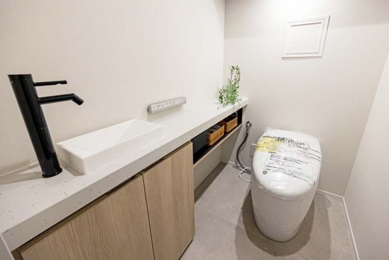 【トイレ】タンクレスの温水洗浄機能付きトイレで、お手入れもしやすくすっきりしています。室内は清潔感があり落ち着く上質な空間です。吊戸棚も設置されており、トイレットペーパーやタオルなどの収納ができます。カウンター付きの便利な専用手洗いスペースも設けられています。
