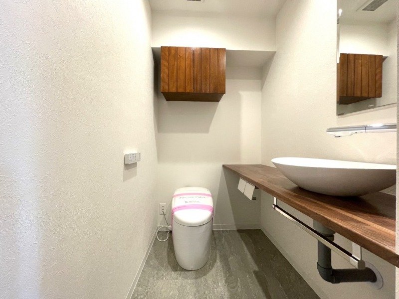 【トイレ】お手入れもしやすいタンクレスで、すっきりとしたデザインの温水洗浄機能付きトイレです。室内は清潔感があり落ち着く上質な空間です。トイレットペーパーなどが収納できる吊戸棚も設置されています。ミラー付きの便利な専用手洗いスペースも設けられています。