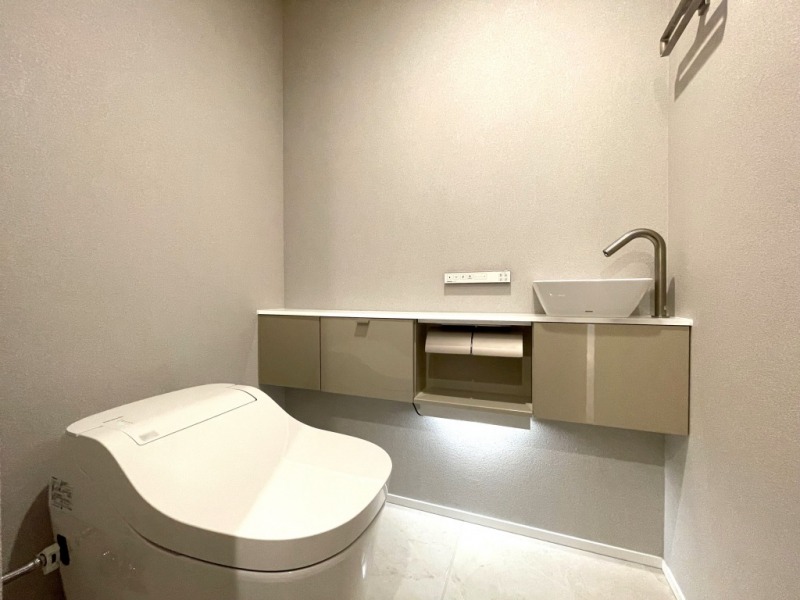 【トイレ】お手入れもしやすいタンクレスで、すっきりとしたデザインの温水洗浄機能付きトイレです。室内は清潔感があり落ち着く上質な空間です。トイレットペーパーなどが収納できる吊戸棚も設置されています。カウンター付きの便利な専用手洗いスペースも設けられています。