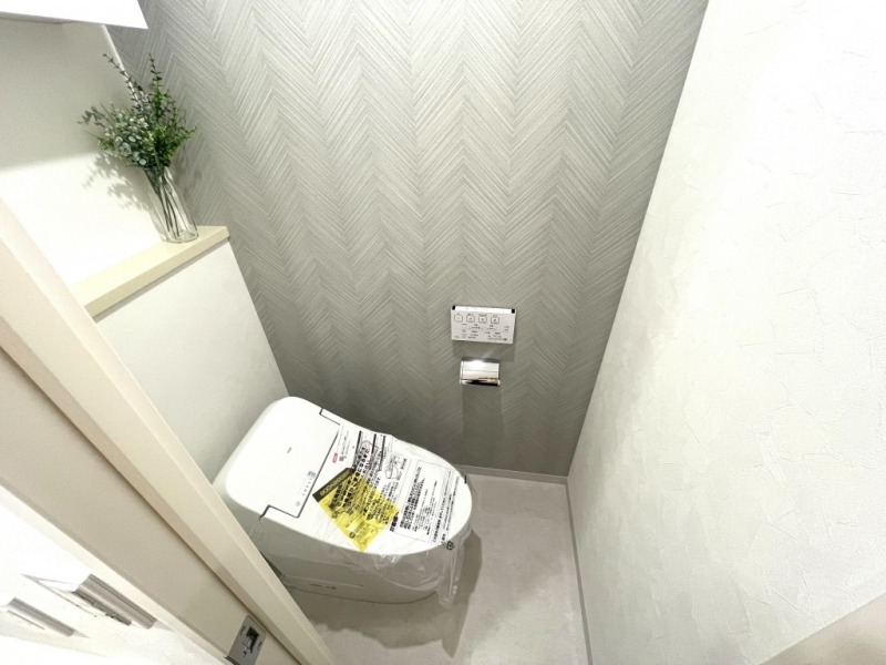 【トイレ】お手入れもしやすいタンクレスで、すっきりとしたデザインの温水洗浄機能付きトイレです。室内はグレーヘリボーンのクロスがアクセントとなった落ち着く上質な空間です。