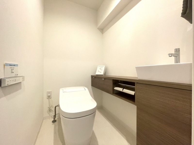 【トイレ】お手入れもしやすいタンクレスで、すっきりとしたデザインの温水洗浄機能付きトイレです。室内は清潔感があり落ち着く上質な空間です。トイレットペーパーなどが収納できる吊戸棚も設置されています。便利な専用手洗いスペースも設けられています。
