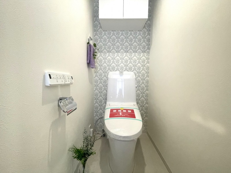 【トイレ】すっきりとしたデザインで清潔感があり、アクセントクロスがおしゃれな空間です。トイレもうれしい洗浄機能付きです。吊戸棚も設置されており、トイレットペーパーなどが収納できます。