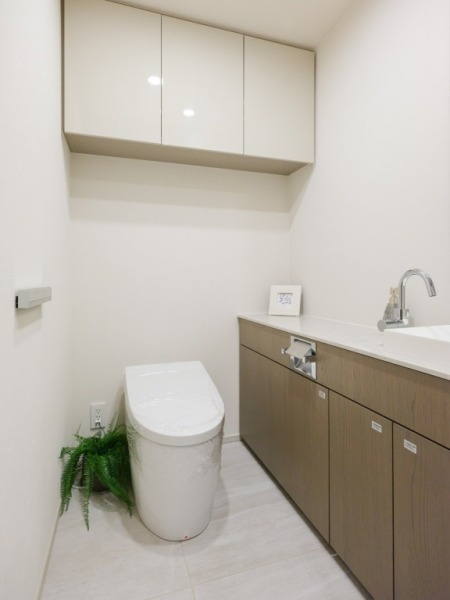 【トイレ】お手入れもしやすいタンクレスで、すっきりとしたデザインの温水洗浄機能付きトイレです。室内は清潔感があり落ち着く上質な空間です。トイレットペーパーなどが収納できる吊戸棚も設置されています。カウンター付きの便利な専用手洗いスペースも設けられています。