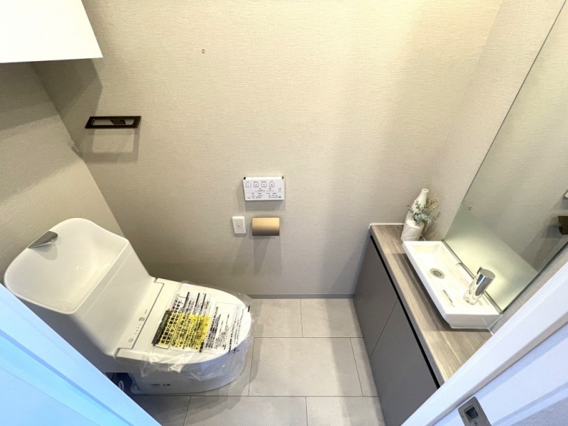 【トイレ】すっきりとしたデザインで清潔感があり、落ち着ける空間です。トイレもうれしい洗浄機能付きです。吊戸棚も設置されており、トイレットペーパーなどが収納できます。ミラー付きの便利な専用手洗いスペースも設けられています。