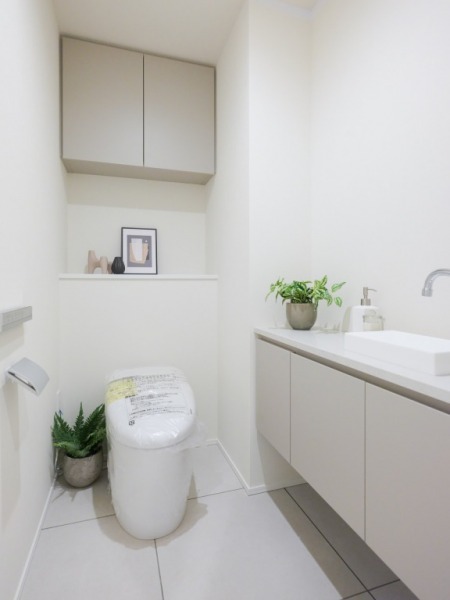 【トイレ】お手入れのしやすいタンクレスで、すっきりとしたデザインの温水洗浄機能付きトイレです。室内は清潔感があり落ち着く上質な空間です。トイレットペーパーなどが収納できる吊戸棚も設置されています。便利な専用手洗いスペースも設けられています。