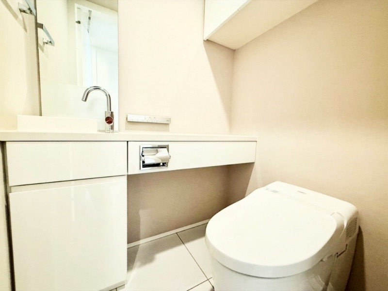 【トイレ】お手入れのしやすいタンクレスで、すっきりとしたデザインの温水洗浄機能付きトイレです。室内は清潔感があり落ち着く上質な空間です。トイレットペーパーなどが収納できる吊戸棚も設置されています。ミラーとカウンター付きの便利な専用手洗いスペースも設けられています。