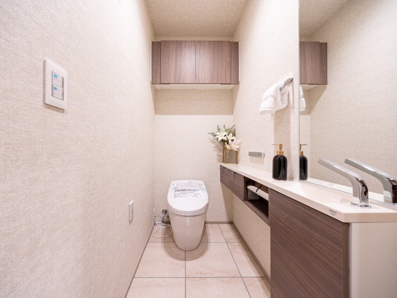 【トイレ】お手入れのしやすいタンクレスで、すっきりとしたデザインの温水洗浄機能付きトイレです。室内は清潔感があり落ち着く上質な空間です。トイレットペーパーなどが収納できる吊戸棚も設置されています。ミラーとカウンター付きの便利な専用手洗いスペースも設けられています。