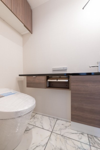 【トイレ】お手入れのしやすいタンクレスで、すっきりとしたデザインの温水洗浄機能付きトイレです。室内は清潔感があり落ち着く上質な空間です。トイレットペーパーなどが収納できる吊戸棚も設置されています。カウンター付きの便利な専用手洗いスペースも設けられています。