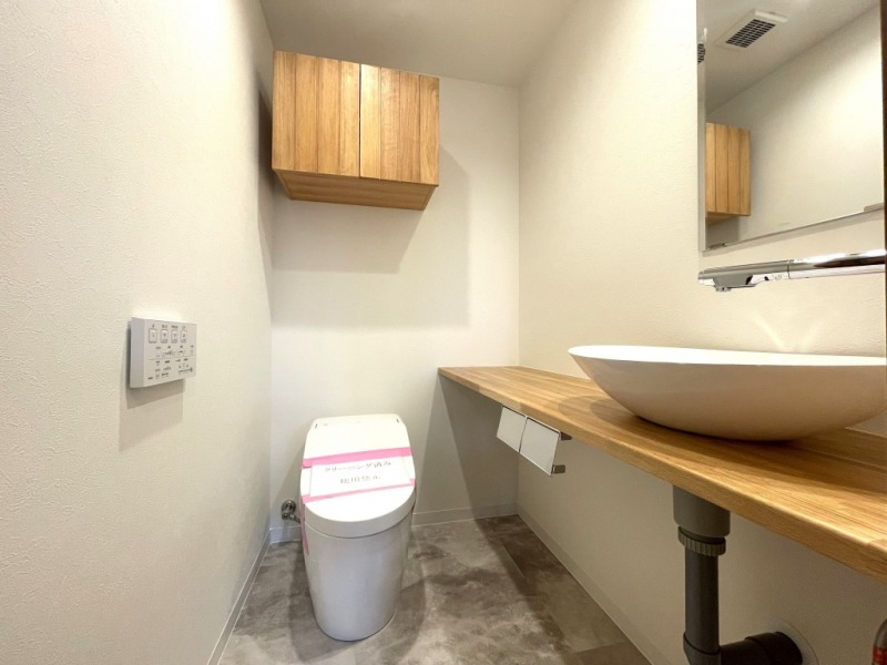 【トイレ】お手入れのしやすいタンクレスで、すっきりとしたデザインの温水洗浄機能付きトイレです。室内は清潔感があり落ち着く上質な空間です。トイレットペーパーなどが収納できる吊戸棚も設置されています。ミラーとカウンター付きの便利な専用手洗いスペースも設けられています。