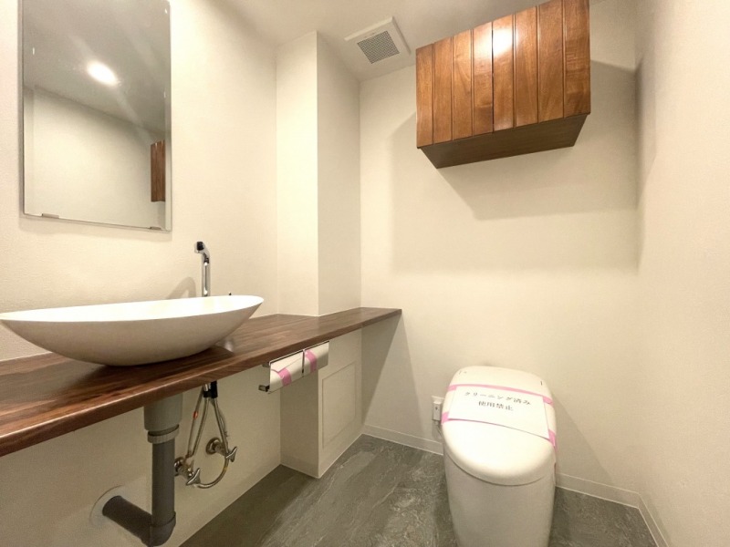 【トイレ】タンクレスですっきりとしたデザインの温水洗浄機能付きトイレです。吊戸棚も設置されており、トイレットペーパーやタオルなどの収納ができます。ミラーとカウンター付の便利な専用手洗いスペースが設けられています。