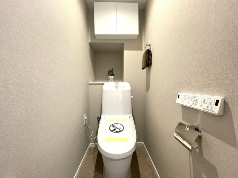 【トイレ】すっきりとしたデザインで清潔感があり、落ち着ける空間です。トイレもうれしい洗浄機能付きです。吊戸棚も設置されており、トイレットペーパーなどが収納できます。