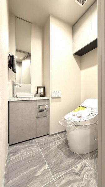 【トイレ】お手入れのしやすいタンクレスで、すっきりとしたデザインの温水洗浄機能付きトイレです。室内は清潔感があり落ち着く上質な空間です。トイレットペーパーなどが収納できる吊戸棚も設置されています。ミラー付きの便利な専用手洗いスペースも設けられています。