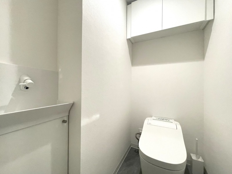 【トイレ】お手入れのしやすいタンクレスで、すっきりとしたデザインの温水洗浄機能付きトイレです。室内は清潔感があり落ち着く上質な空間です。トイレットペーパーなどが収納できる吊戸棚も設置されています。便利な専用手洗いスペースも設けられています。