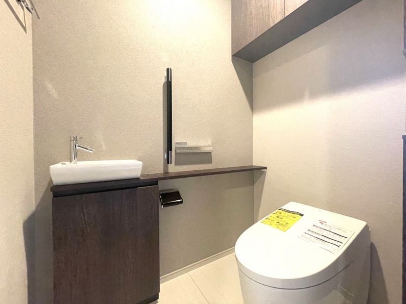 【トイレ】お手入れのしやすいタンクレスで、すっきりとしたデザインの温水洗浄機能付きトイレです。室内は清潔感があり落ち着く上質な空間です。トイレットペーパーなどが収納できる吊戸棚も設置されています。便利なカウンター付き専用手洗いスペースも設けられています。