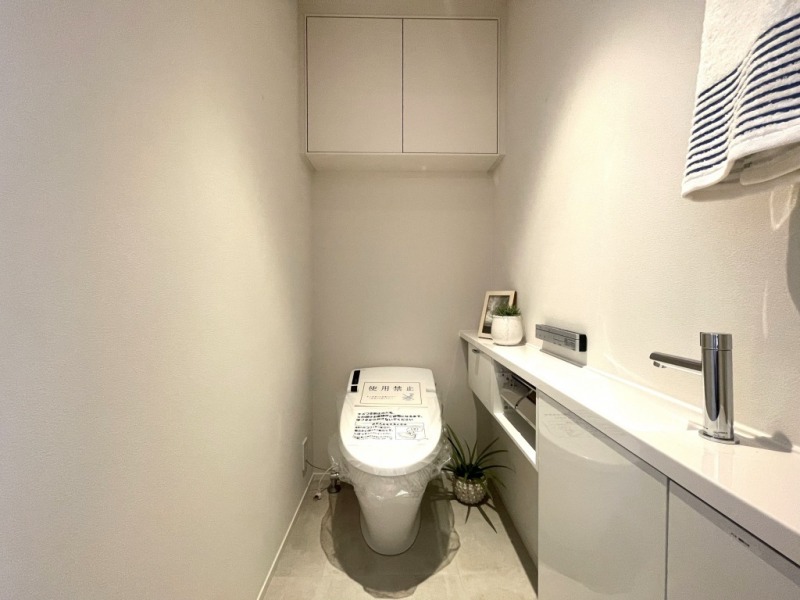 【トイレ】お手入れのしやすいタンクレスで、すっきりとしたデザインの温水洗浄機能付きトイレです。室内は清潔感があり落ち着く上質な空間です。トイレットペーパーなどが収納できる吊戸棚も設置されています。カウンター付きの便利な専用手洗いスペースも設けられています。