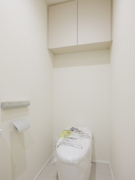【トイレ】お手入れのしやすいタンクレスで、すっきりとしたデザインの温水洗浄機能付きトイレです。室内は清潔感があり落ち着く上質な空間です。トイレットペーパーなどが収納できる吊戸棚も設置されています。便利な専用手洗いスペースも設けられています。