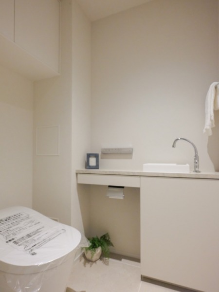 【トイレ】お手入れのしやすいタンクレスで、すっきりとしたデザインの温水洗浄機能付きトイレです。室内は清潔感があり落ち着く上質な空間です。トイレットペーパーなどが収納できる吊戸棚も設置されています。カウンター付きの便利な専用手洗いスペースも設けられています。
