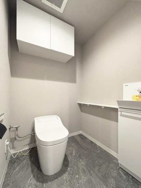 【トイレ】お手入れのしやすいタンクレスで、すっきりとしたデザインの温水洗浄機能付きトイレです。室内は清潔感があり落ち着く上質な空間です。トイレットペーパーなどが収納できる吊戸棚も設置されています。便利な専用手洗いスペースも設けられています。