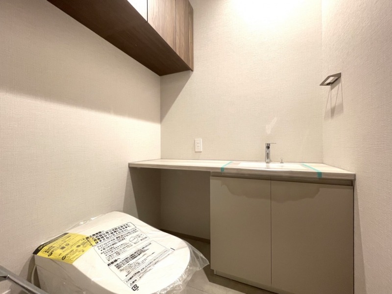 【トイレ】お手入れのしやすいタンクレスで、すっきりとしたデザインの温水洗浄機能付きトイレです。室内は清潔感があり落ち着く上質な空間です。トイレットペーパーなどが収納できる吊戸棚も設置されています。カウンターの付いた便利な専用手洗いスペースも設けられています。