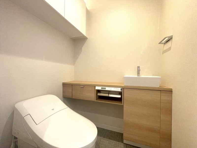 【トイレ】お手入れのしやすいタンクレスで、すっきりとしたデザインの温水洗浄機能付きトイレです。室内は清潔感があり落ち着く上質な空間です。トイレットペーパーなどが収納できる吊戸棚も設置されています。カウンター付きの便利な専用手洗いスペースも設けられています。