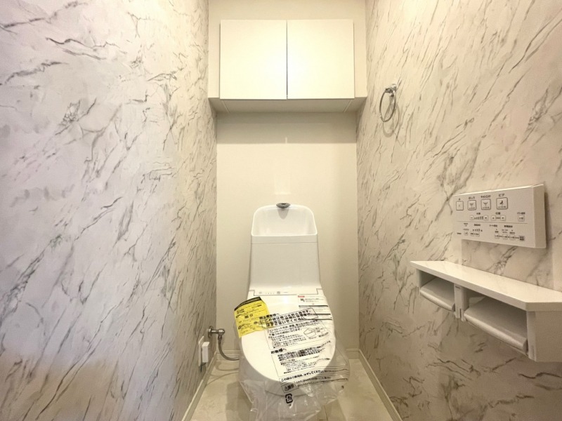 【トイレ】洗面室とデザインが統一された空間です。トイレもうれしいウォシュレット機能付きです。吊戸棚も設置されており、トイレットペーパーなどが収納できます。