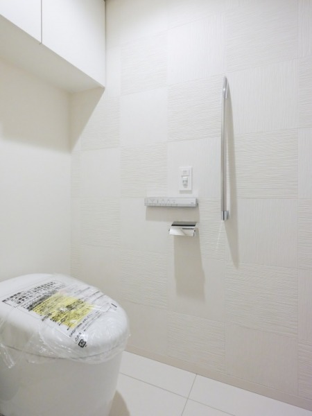 【トイレ】洗面室に隣接したトイレです。お手入れのしやすいタンクレスで、すっきりとしたデザインの温水洗浄機能付きトイレです。室内はホワイトを基調とし、清潔感のある落ち着く空間です。トイレットペーパーなどが収納できる吊戸棚も設置されています。