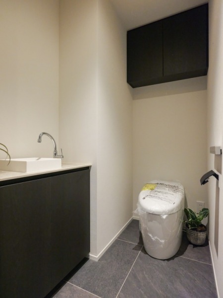 【トイレ】お手入れのしやすいタンクレスで、すっきりとしたデザインの温水洗浄機能付きトイレです。室内は清潔感があり落ち着く上質な空間です。トイレットペーパーなどが収納できる吊戸棚も設置されています。便利な専用手洗いスペースも設けられています。