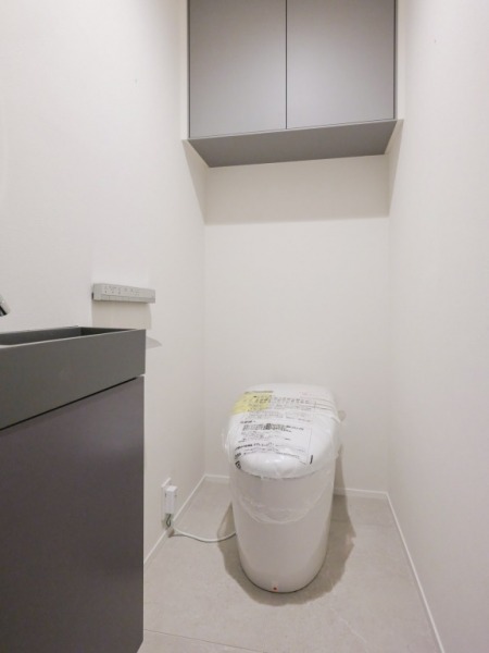 【トイレ】お手入れのしやすいタンクレスで、すっきりとしたデザインの温水洗浄機能付きトイレです。室内は清潔感があり落ち着く上質な空間です。トイレットペーパーなどが収納できる吊戸棚も設置されています。便利な専用手洗いスペースも設けられています。