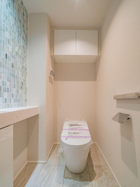 【トイレ】お手入れのしやすいタンクレスで、すっきりとしたデザインの温水洗浄機能付きトイレです。室内は洗面室とデザインが統一されていて、清潔感があり落ち着く上質な空間です。トイレットペーパーなどが収納できる吊戸棚も設置されています。カウンター付きの便利な専用手洗いスペースも設けられています。