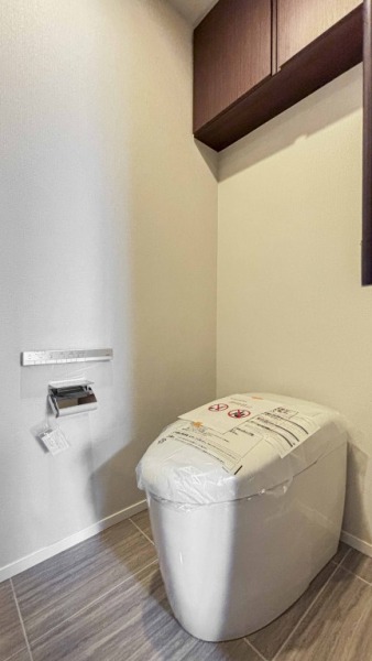【トイレ】お手入れのしやすいタンクレスで、すっきりとしたデザインの温水洗浄機能付きトイレです。室内は清潔感があり落ち着く上質な空間です。トイレットペーパーなどが収納できる吊戸棚も設置されています。便利な専用手洗いスペースも設けられています。