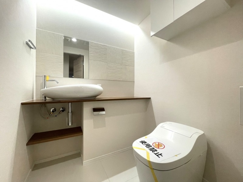 【トイレ】お手入れのしやすいタンクレスで、すっきりとしたデザインの温水洗浄機能付きトイレです。室内は清潔感があり落ち着く上質な空間です。トイレットペーパーなどが収納できる吊戸棚も設置されています。カウンターとミラーの付いた便利な専用手洗いスペースも設けられています。