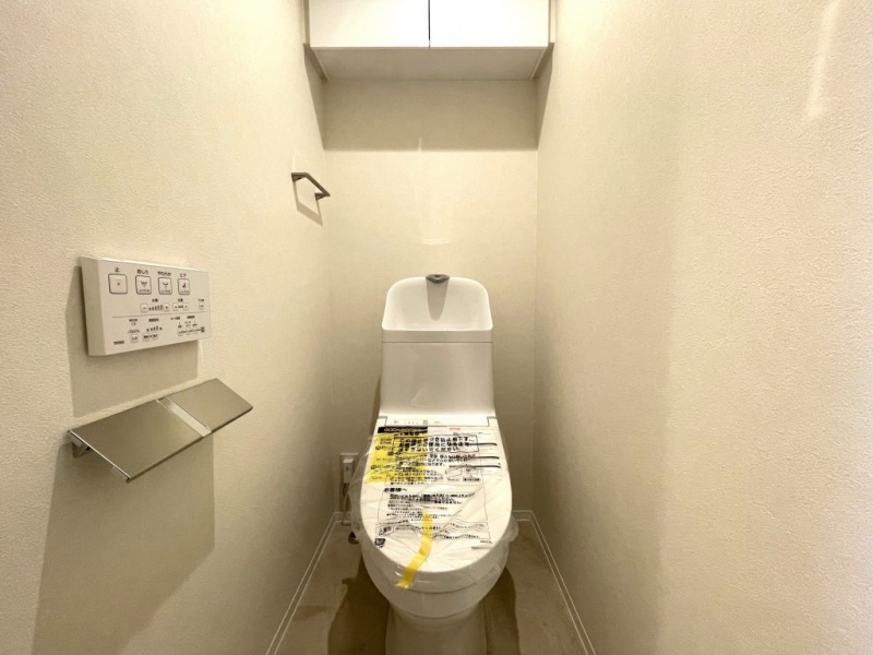 【トイレ】すっきりとしたデザインで清潔感があり、落ち着ける空間です。トイレもうれしい洗浄機能付きです。吊戸棚も設置されており、トイレットペーパーなどが収納できます。