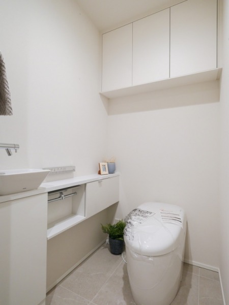 【トイレ】お手入れのしやすいタンクレスで、すっきりとしたデザインの温水洗浄機能付きトイレです。室内は清潔感があり落ち着く上質な空間です。トイレットペーパーなどが収納できる吊戸棚も設置されています。カウンター付きの便利な専用手洗いスペースも設けられています。