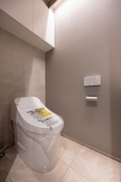 【トイレ】お手入れのしやすいタンクレスで、すっきりとしたデザインの温水洗浄機能付きトイレです。室内は清潔感があり落ち着く上質な空間です。トイレットペーパーなどが収納できる吊戸棚も設置されています。