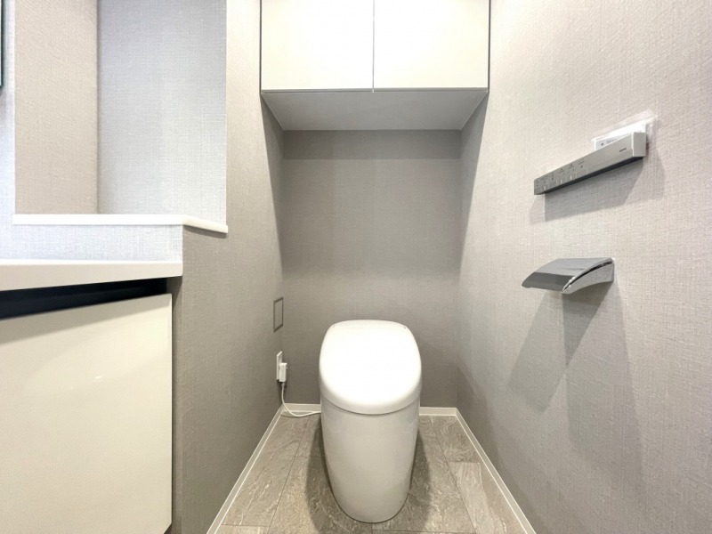 【トイレ】お手入れのしやすいタンクレスで、すっきりとしたデザインの温水洗浄機能付きトイレです。室内は清潔感があり落ち着く上質な空間です。トイレットペーパーなどが収納できる吊戸棚も設置されています。便利な専用手洗いスペースも設けられています。