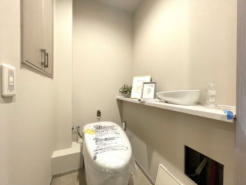 【トイレ】お手入れのしやすいタンクレスで、すっきりとしたデザインの温水洗浄機能付きトイレです。室内は清潔感があり落ち着く上質な空間です。トイレットペーパーなどが収納できる収納棚も設置されています。カウンターと便利な専用手洗いスペースも設けられています。