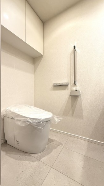 【トイレ】お手入れのしやすいタンクレスで、すっきりとしたデザインの温水洗浄機能付きトイレです。室内は清潔感があり落ち着く上質な空間です。トイレットペーパーなどが収納できる吊戸棚も設置されています。便利な専用手洗いスペースも設けられています。