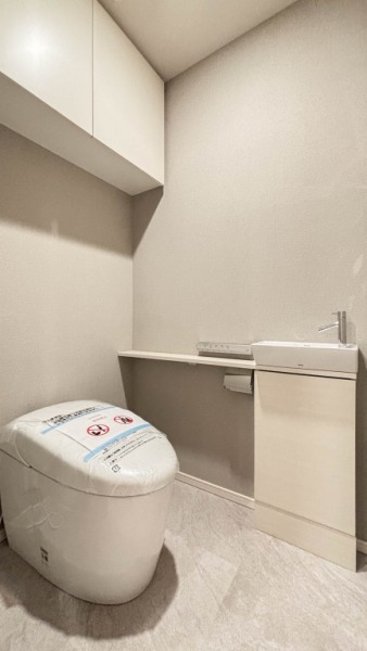 【トイレ】お手入れのしやすいタンクレスで、すっきりとしたデザインの温水洗浄機能付きトイレです。室内は清潔感があり落ち着く上質な空間です。トイレットペーパーなどが収納できる吊戸棚も設置されています。便利な専用手洗いスペースも設けられています。