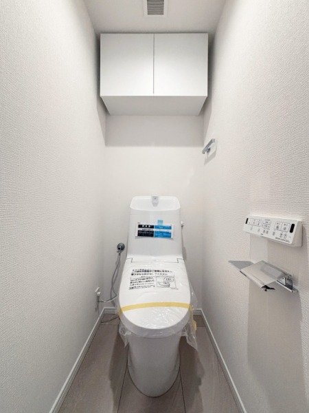 【トイレ】すっきりとしたデザインで清潔感があり、落ち着ける空間です。トイレもうれしい洗浄機能付きです。吊戸棚も設置されており、トイレットペーパーなどが収納できます。