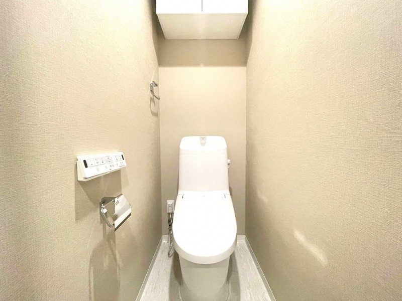 【トイレ】すっきりとしたデザインで清潔感があり、落ち着ける空間です。トイレもうれしい洗浄機能付きです。吊戸棚も設置されており、トイレットペーパーなどが収納できます。