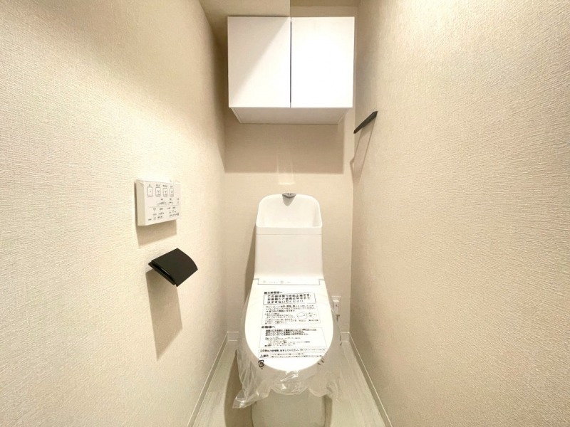【トイレ】すっきりとしたデザインで清潔感があり、落ち着ける空間です。トイレもうれしい洗浄機能付きです。吊戸棚も設置されており、トイレットペーパーなどが収納できます。
