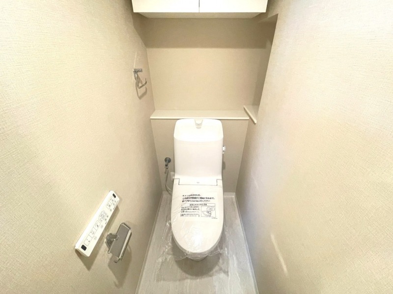 【トイレ】すっきりとしたデザインで清潔感があり、落ち着ける空間です。トイレもうれしい洗浄機能付きです。吊戸棚も設置されており、トイレットペーパーなどが収納できます。