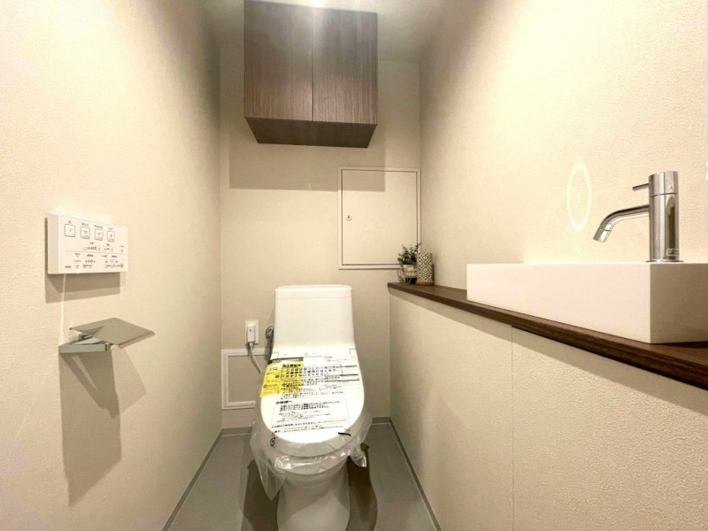 【トイレ】すっきりとしたデザインで清潔感があり、落ち着ける空間です。トイレもうれしい洗浄機能付きです。吊戸棚も設置されており、トイレットペーパーなどが収納できる吊戸棚を備え、カウンター付きの便利な専用手洗いスペースも設けられています。