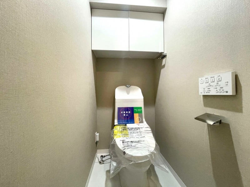 【トイレ】すっきりとしたデザインで清潔感があり、落ち着ける空間です。トイレもうれしい洗浄機能付きです。吊戸棚も設置されており、トイレットペーパーなどが収納できます。