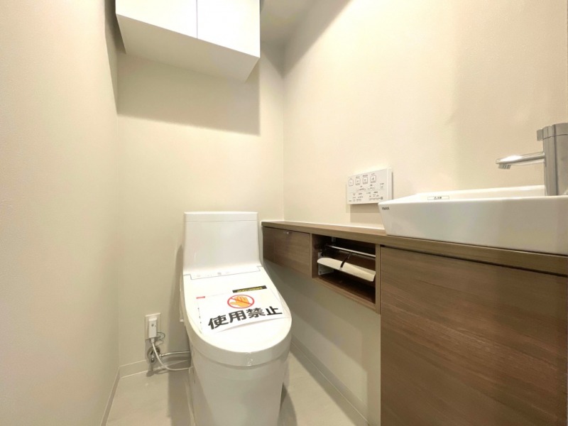 【トイレ】すっきりとしたデザインで清潔感があり、落ち着ける空間です。トイレもうれしい洗浄機能付きです。吊戸棚も設置されており、トイレットペーパーなどが収納できます。カウンター付きの便利な専用手洗いスペースも設けられています。
