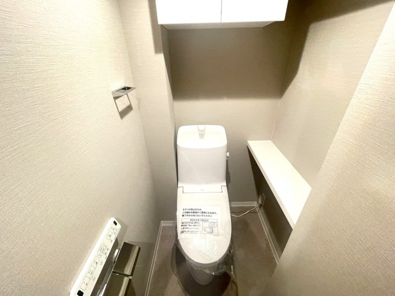 【トイレ】すっきりとしたデザインで清潔感があり、落ち着ける空間です。トイレもうれしい洗浄機能付きです。吊戸棚も設置されており、トイレットペーパーなどが収納できます。
