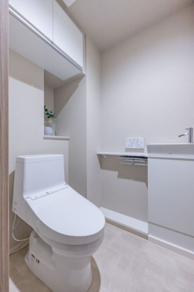 【トイレ】すっきりとしたデザインで清潔感があり、落ち着ける空間です。トイレもうれしい洗浄機能付きです。吊戸棚も設置されており、トイレットペーパーなどが収納できます。便利な専用手洗いスペースも設けられています。