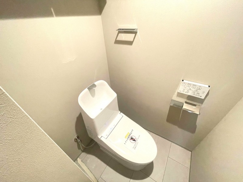 【トイレ】すっきりとしたデザインで清潔感があり、落ち着ける空間です。トイレもうれしい洗浄機能付きです。吊戸棚も設置されており、トイレットペーパーなどが収納できます。