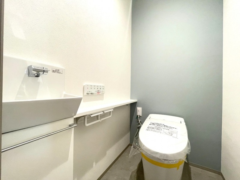 【トイレ】お手入れのしやすいタンクレスで、すっきりとしたデザインの温水洗浄機能付きトイレ。室内は清潔感があり落ち着く上質な空間です。トイレットペーパーなどが収納できる吊戸棚を備え、便利な専用手洗いスペースも設けられています。