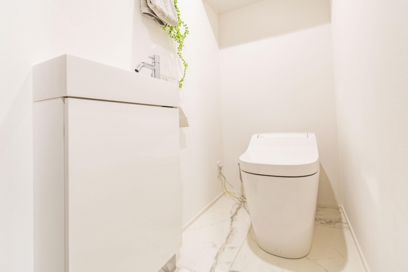 【トイレ】お手入れもしやすいタンクレスのすっきりとしたデザインの温水洗浄機能付きトイレです。室内はホワイトを基調とし、清潔感のある落ち着く空間です。トイレットペーパーなどが収納できる吊戸棚も設置されています。便利な専用手洗いスペースも設けられています。